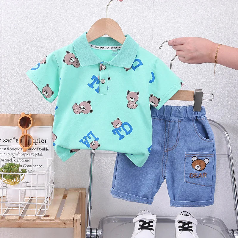 Children's outfit with a green shirt and blue shorts on a hanger against a white background.
