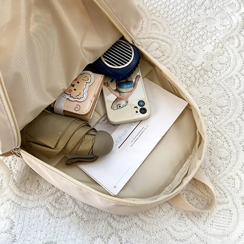 Beige backpack with items including a phone, umbrella, and documents on a textured surface