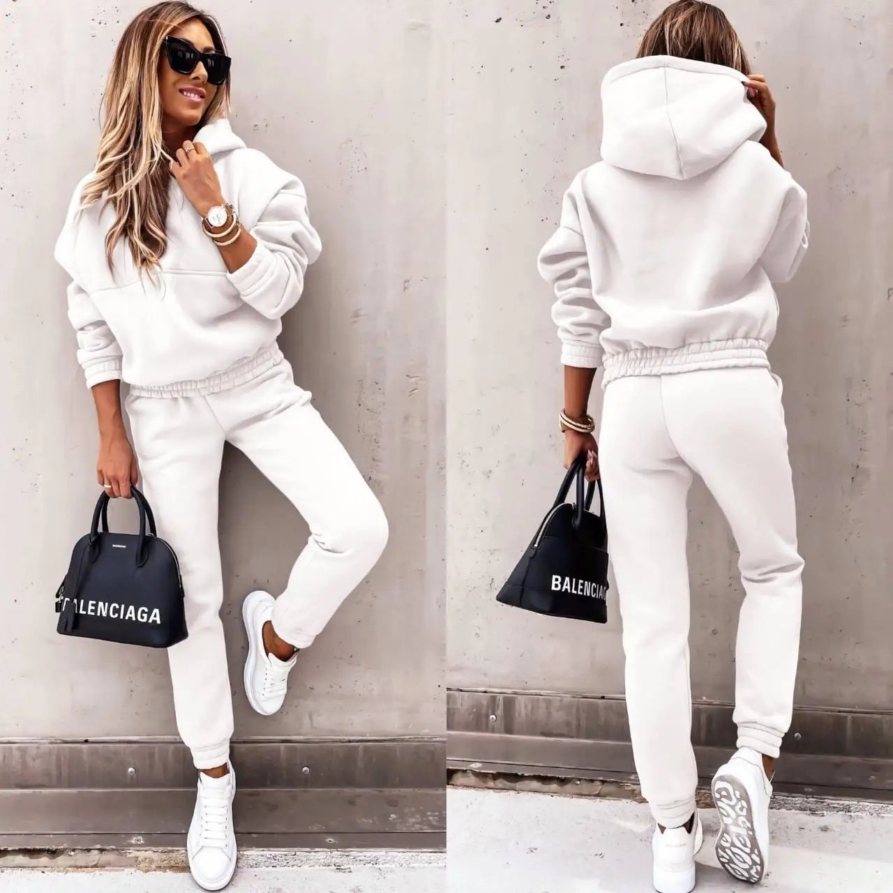 Woman wearing a white tracksuit with a Balenciaga bag against a gray wall.