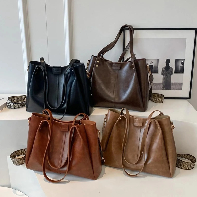 Four leather handbags in black, brown, and two shades of brown on a white surface.