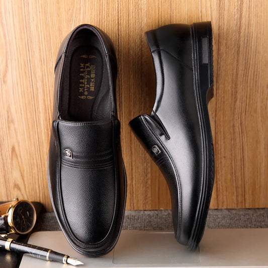 Pair of black leather shoes on a wooden surface with a pen and notebook.