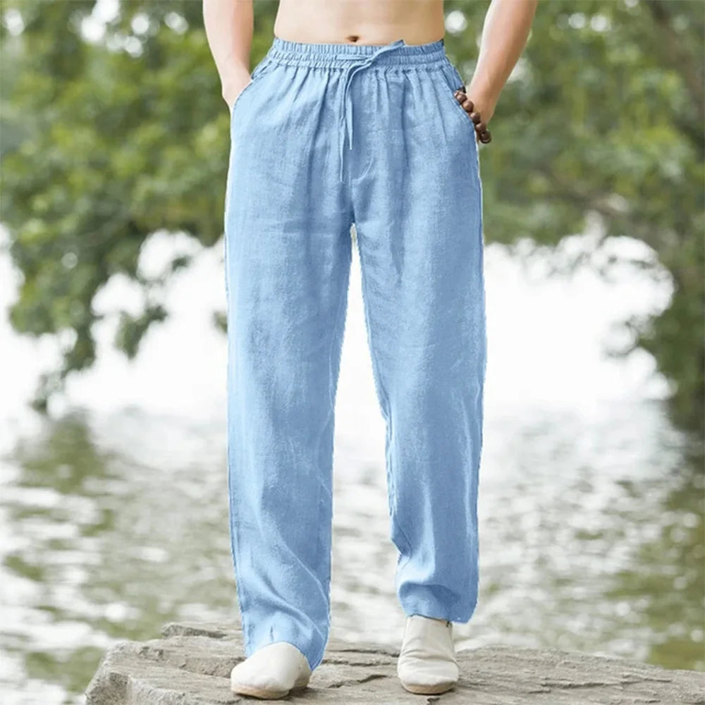 Person wearing light blue pants standing by a water body with greenery.