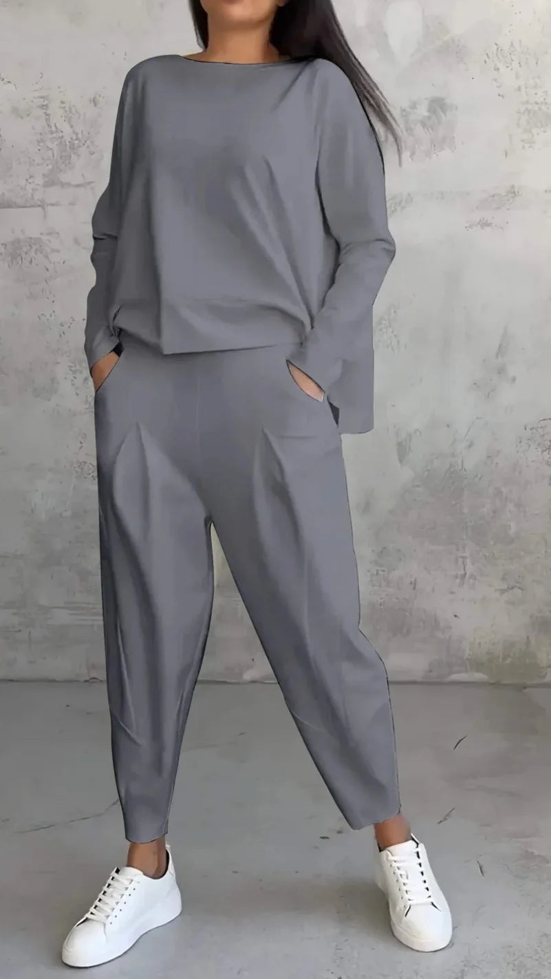 Person wearing a gray outfit with white sneakers against a concrete wall.