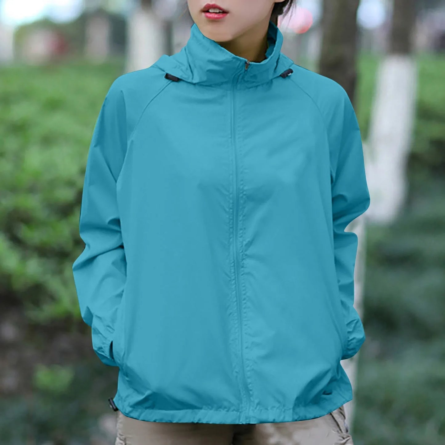 Person wearing a teal jacket outdoors with a blurred green background