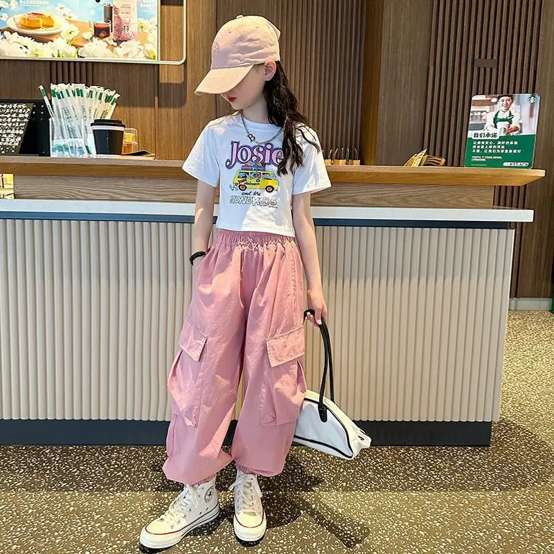 Child wearing a white t-shirt with graphics and pink pants standing in front of a counter.