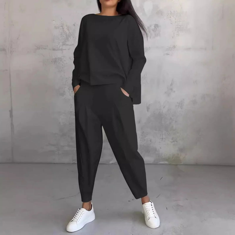 Person wearing a black outfit with white sneakers against a gray concrete wall.