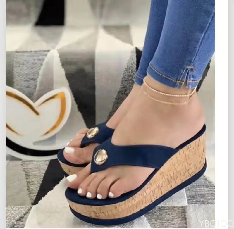 Navy wedge sandals with gold buttons worn by a person on a patterned rug.