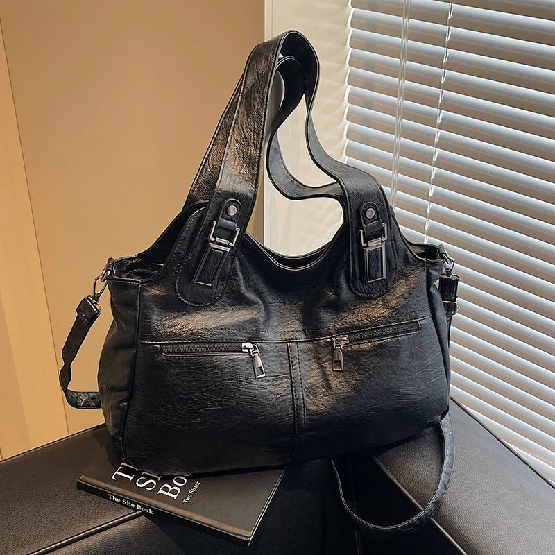 Black leather handbag on a surface with a book underneath, against a window with blinds.