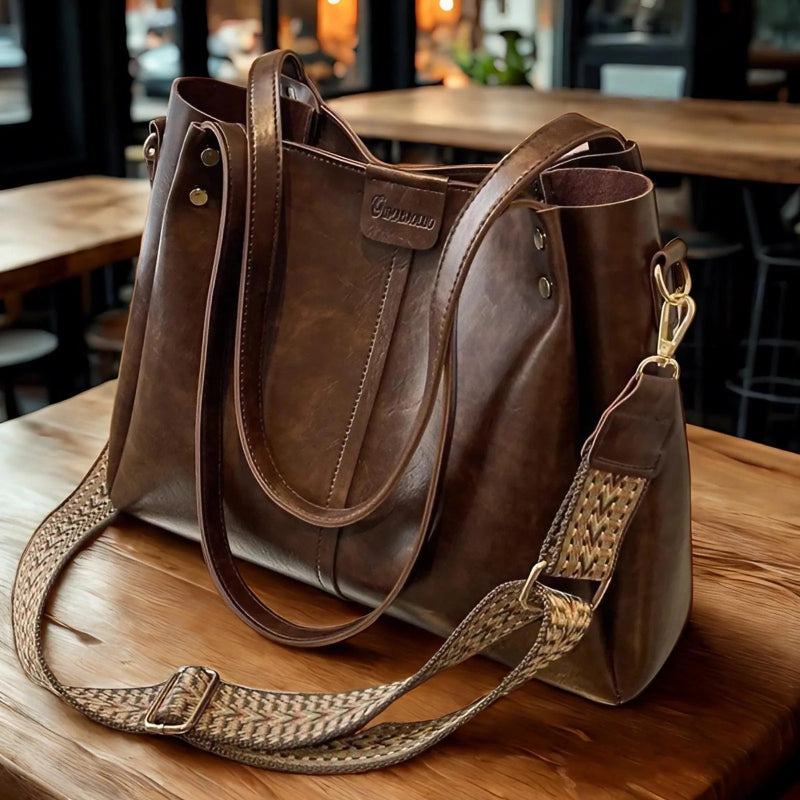 Brown leather handbag with a woven strap on a wooden table.