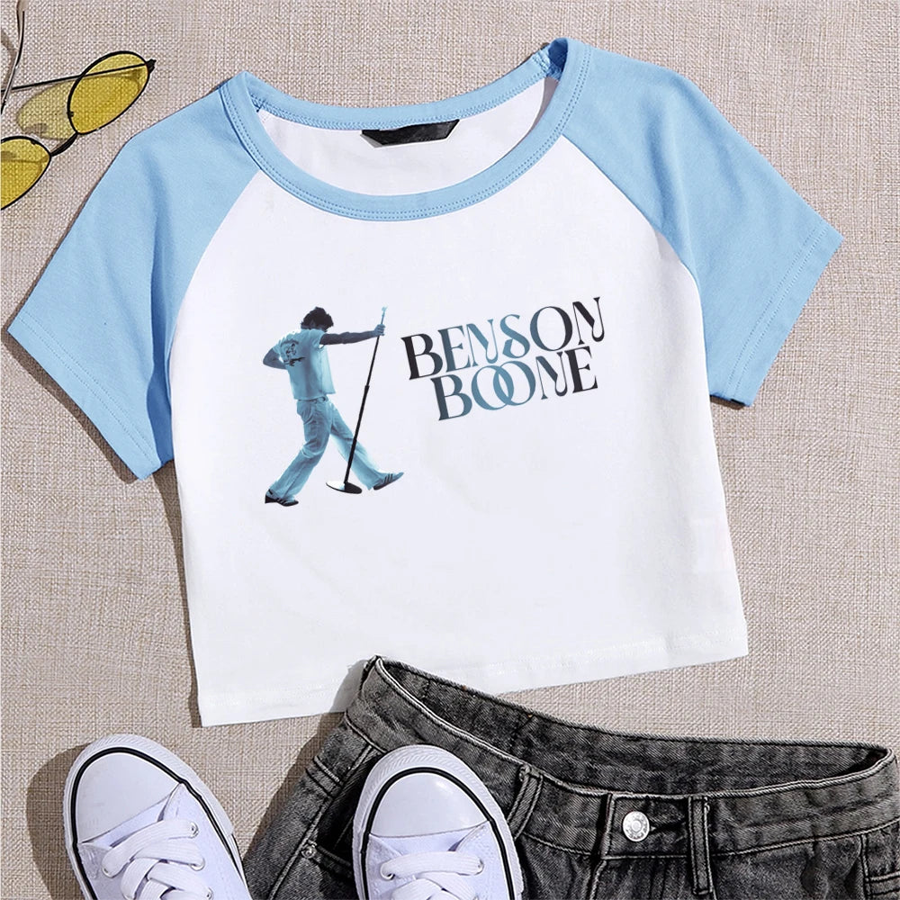 White and blue t-shirt with 'Benson Boone' graphic and text, paired with jeans and sneakers on a textured surface.