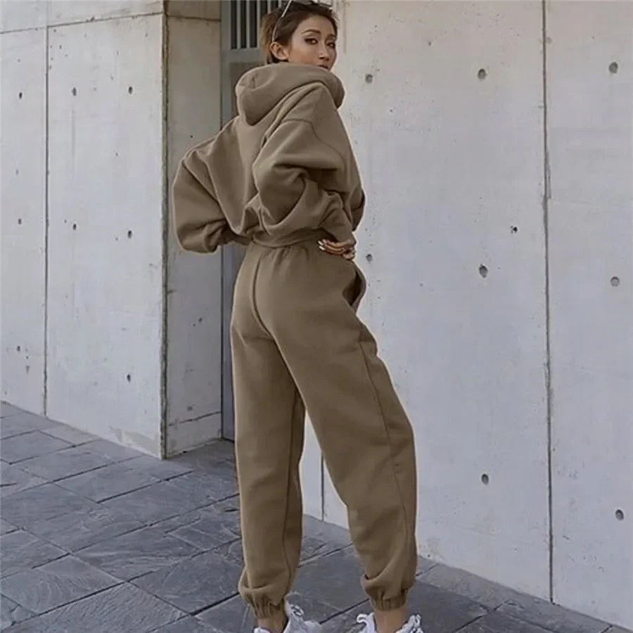 Person wearing a beige tracksuit standing against a concrete wall.