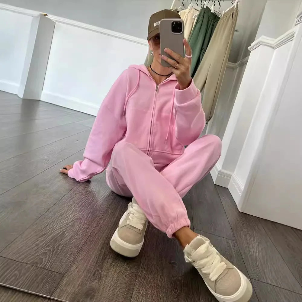 Person wearing a pink tracksuit sitting on the floor in a room with white walls and wooden flooring.