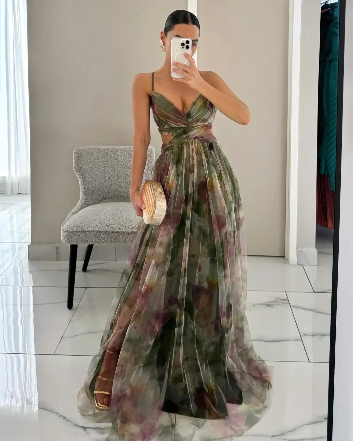 Woman in a floral dress taking a mirror selfie in an indoor setting.