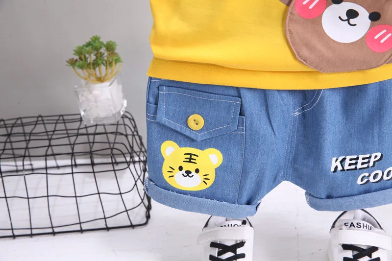 Child's outfit with denim shorts featuring a tiger patch, yellow shirt with bear design, and white sneakers.