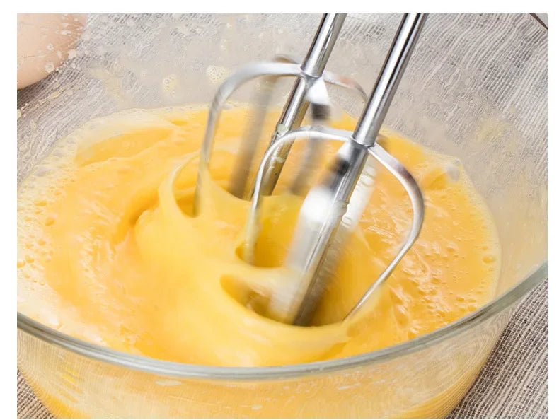 Yellow mixture being stirred with a hand mixer in a glass bowl.