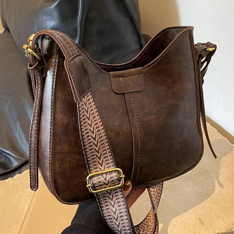 Brown leather handbag with a patterned strap held by a person.
