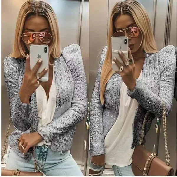 Woman taking a mirror selfie wearing a sequined jacket, white top, and denim jeans.
