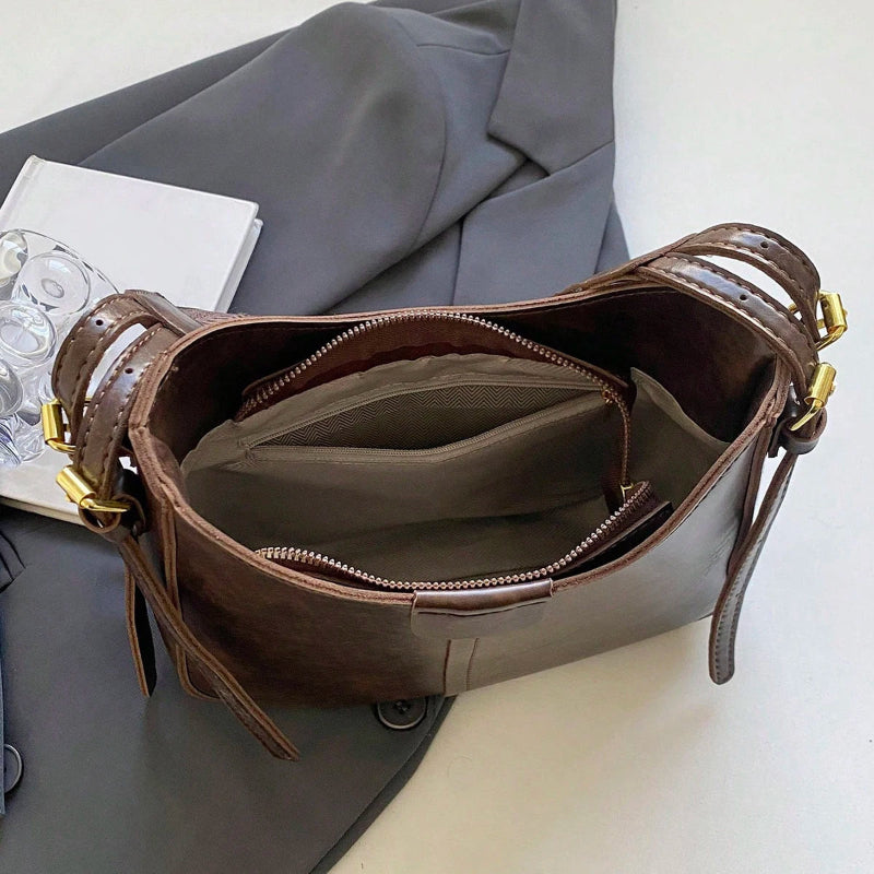 Brown leather handbag with gold accents on a gray surface