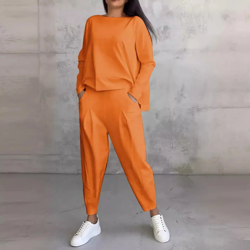 Person wearing an orange outfit with white sneakers against a gray concrete wall.