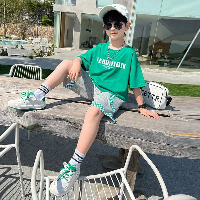 Child sitting on a wooden bench outdoors wearing a green t-shirt and sunglasses.