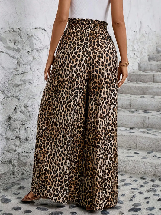 Person wearing leopard print pants standing on a stone path with a white wall background