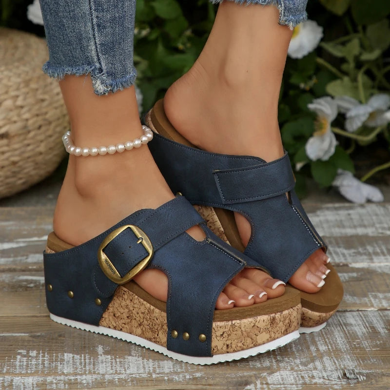 Navy blue sandals with cork platforms worn by a person on a wooden surface with plants in the background.