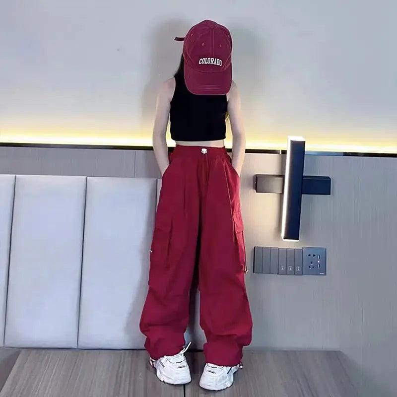 Person wearing a red cap, black crop top, and red pants standing in a modern interior setting.
