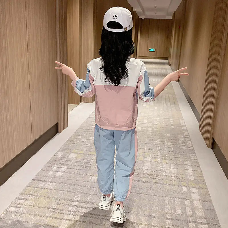 Child wearing a colorful outfit with a cap, standing in a hallway.