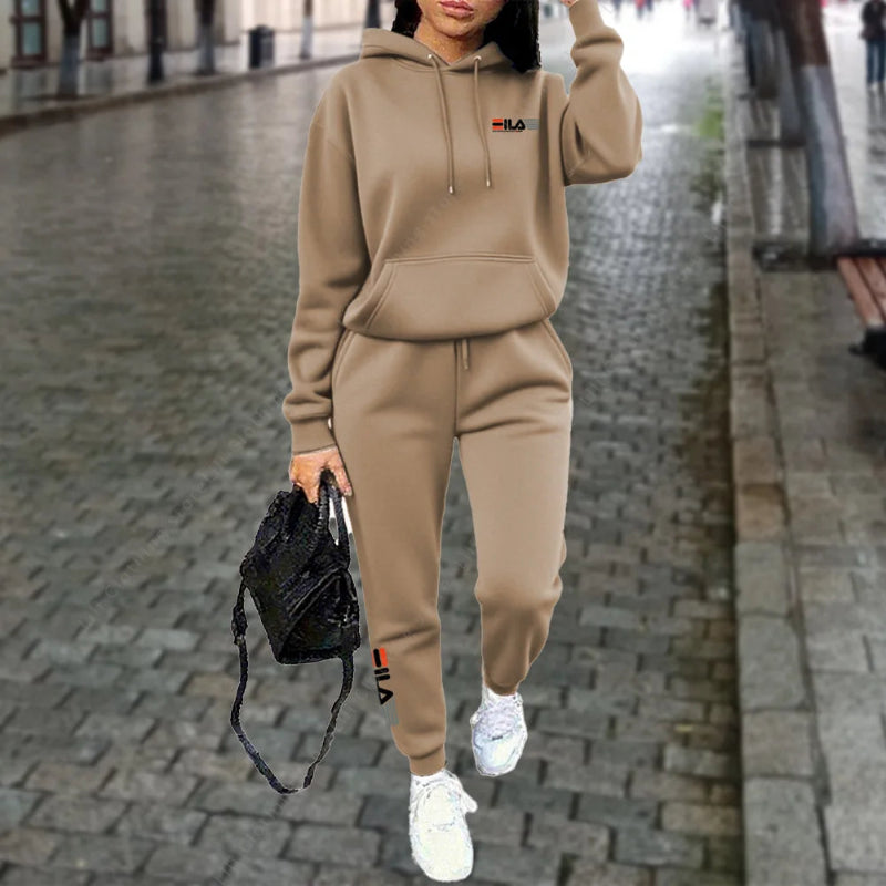 Person wearing a beige hoodie and jogger set on a city street.