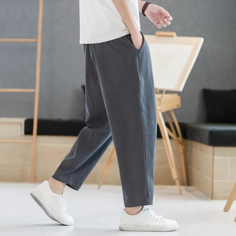 Person wearing gray pants and white sneakers in a room with a gray wall and wooden furniture.