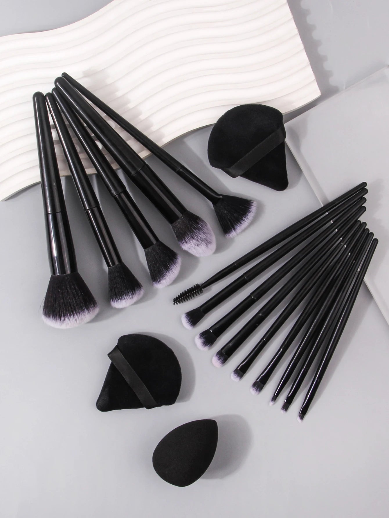 Set of black makeup brushes and tools on a light gray surface