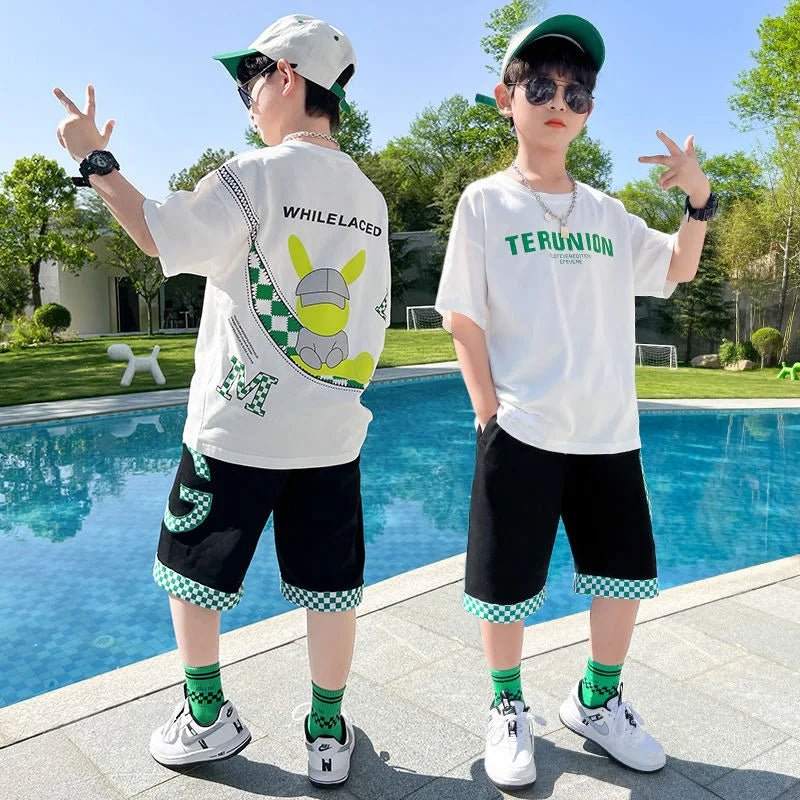 Two children posing by a pool, wearing matching outfits with text and graphics on their shirts.