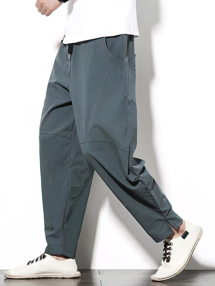 Person wearing gray pants and white sneakers on a plain background