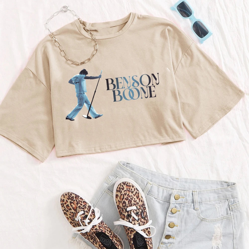 Beige crop top with graphic design, sunglasses, leopard print shoes, and light blue jeans on a white background