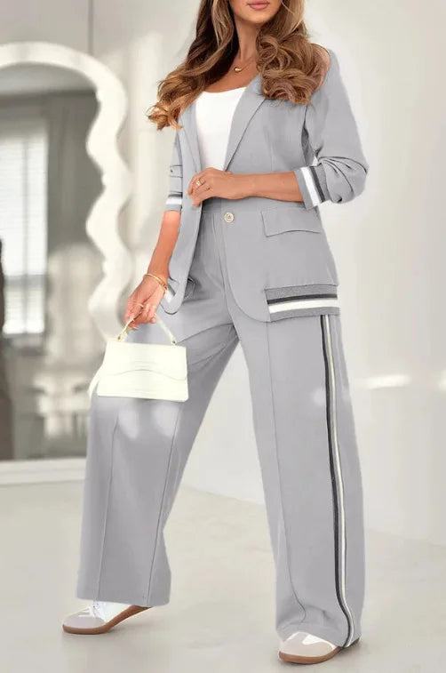 Woman wearing a gray suit with a white top, holding a white handbag indoors.