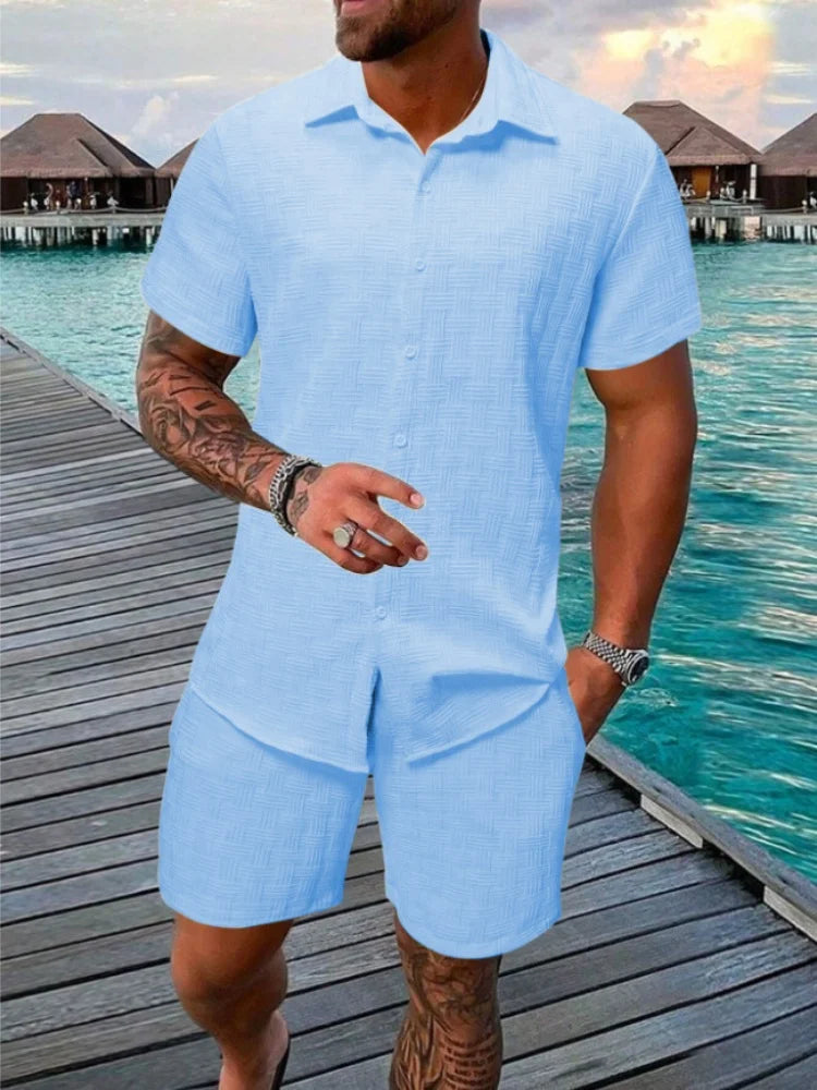 A man wearing a white short-sleeved shirt and matching shorts with a drawstring closure, standing near a poolside.