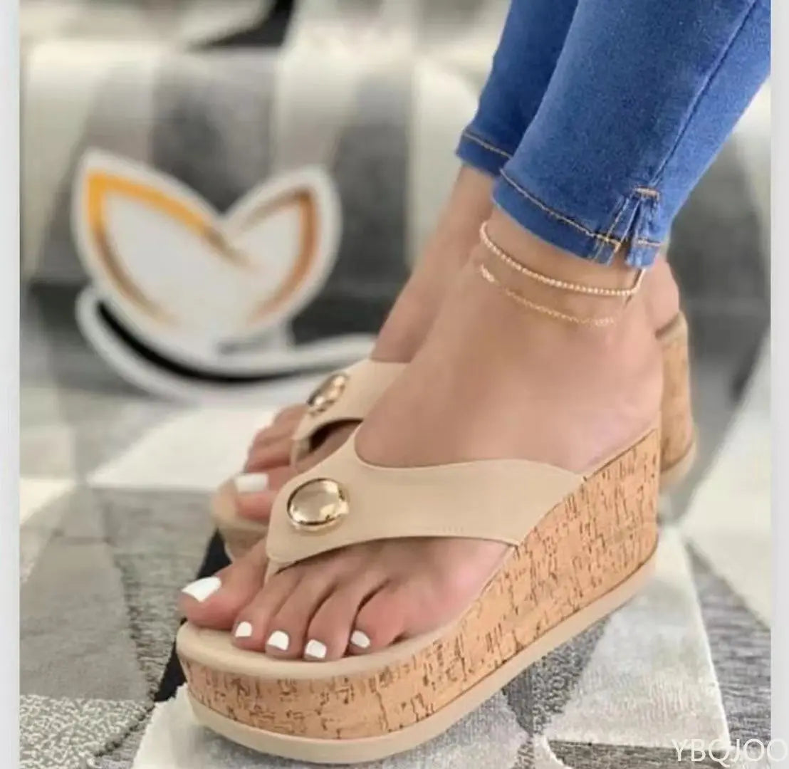 Beige sandals with cork sole worn by a person, with a blurred background of a coffee cup.