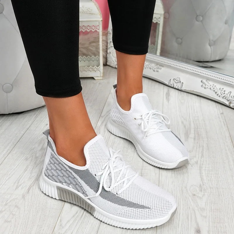 White and gray sneakers worn indoors on a light wooden floor.