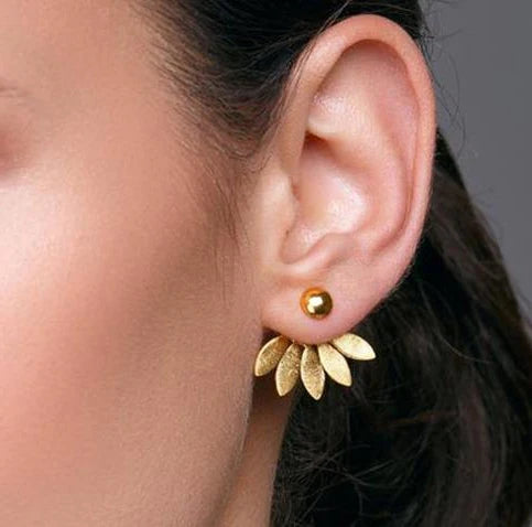 Gold flower-shaped earring worn by a person with a neutral background