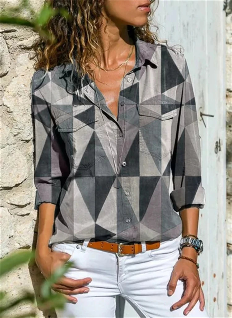 Person wearing a geometric patterned shirt with rolled-up sleeves against a stone wall.