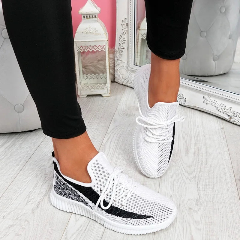White and black sneakers worn indoors on a light wooden floor.