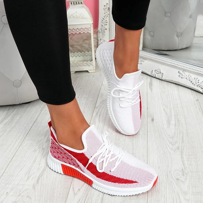 White and red sneakers worn indoors on a light wooden floor.