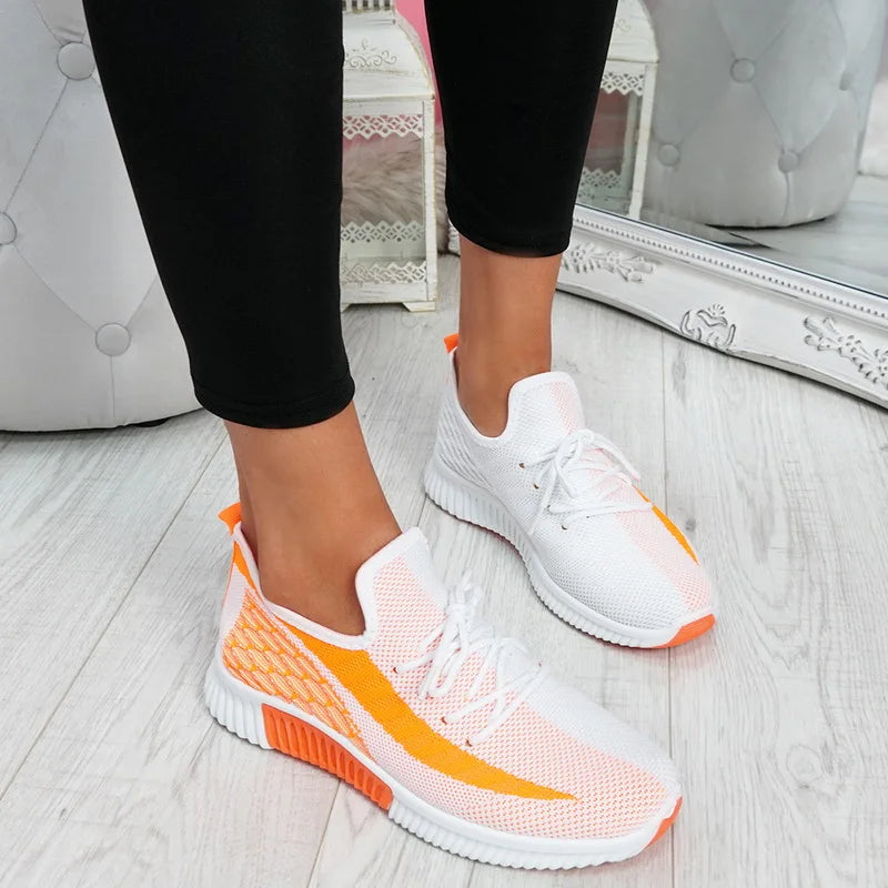 White and orange sneakers worn with black leggings on a light wooden floor.
