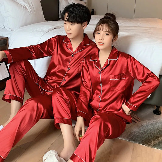 Two people wearing red satin pajamas sitting on a bed.