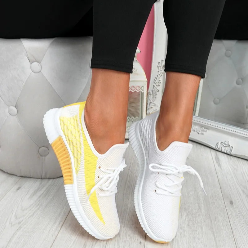 White sneakers with yellow accents worn by a person on a light wooden floor.