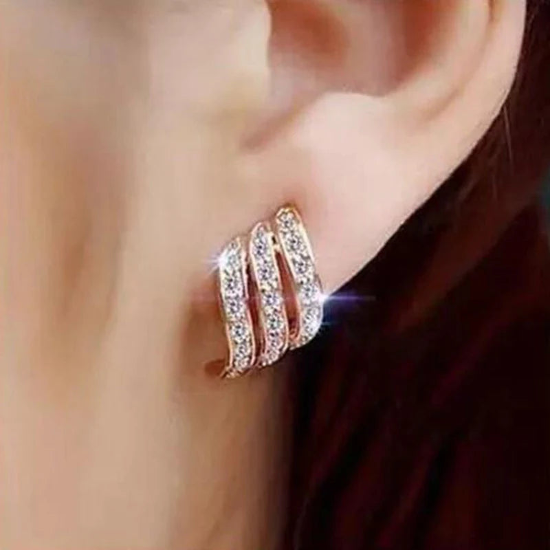 Close-up of an ear wearing a rose gold hoop earring with clear gemstones.