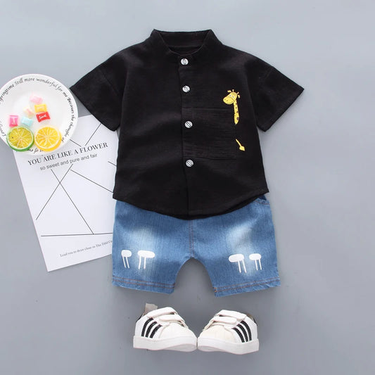 Black shirt with yellow giraffe design, denim shorts, and white sneakers on a gray background