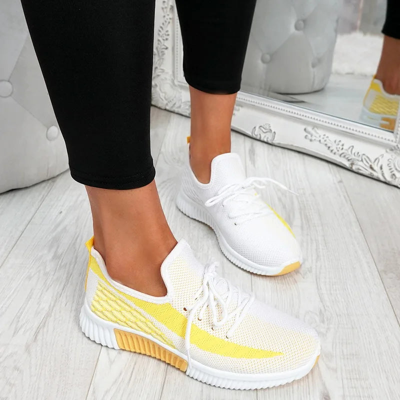 White and yellow sneakers worn with black pants on a light wooden floor.