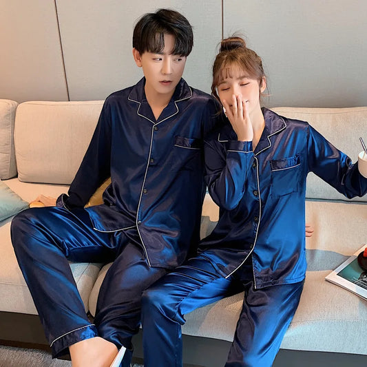 Two people wearing matching blue satin pajamas sitting on a couch.