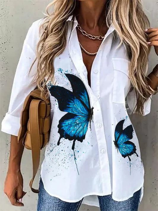 White shirt with blue butterfly designs worn by a person, holding a brown bag.